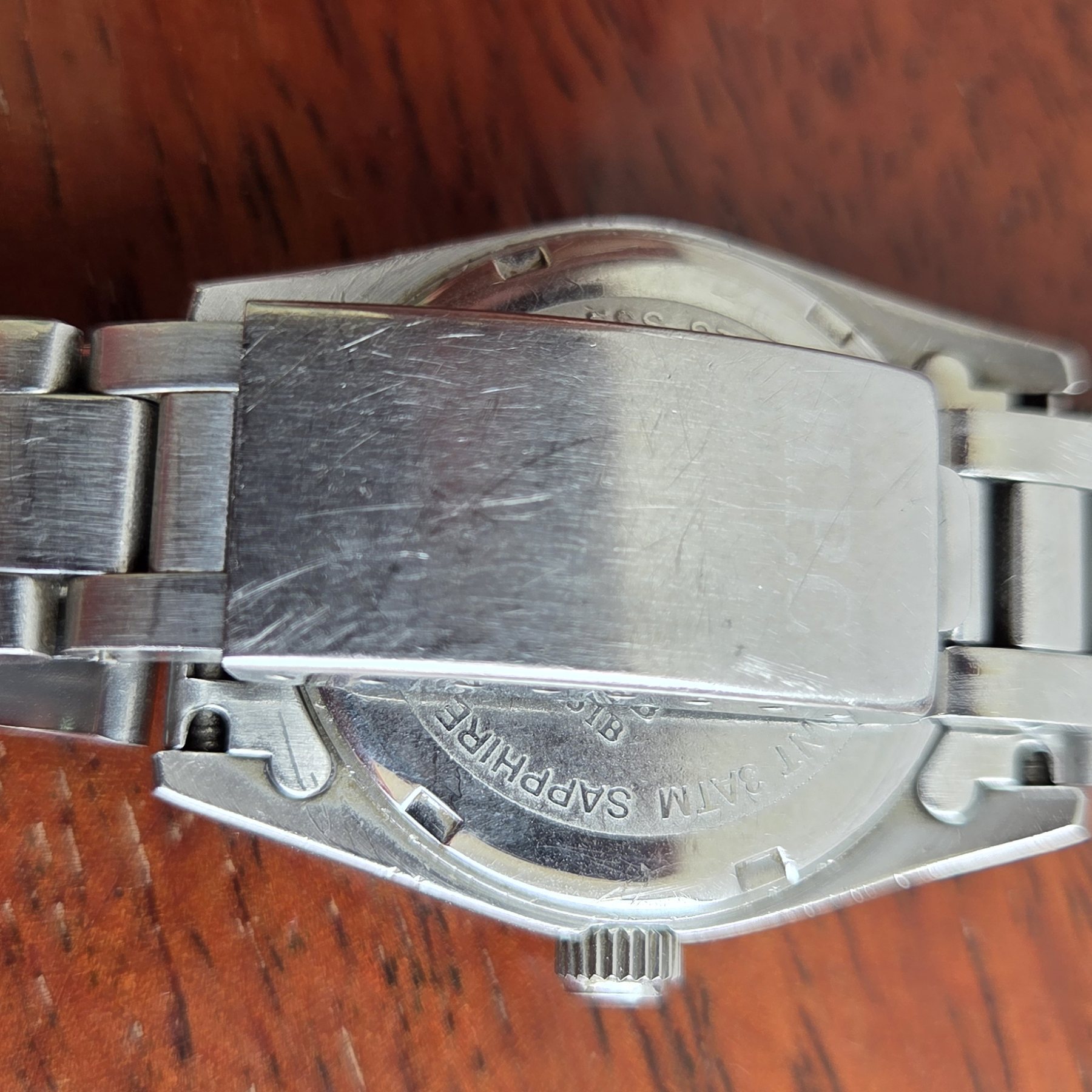 The folding clasp of the steel bracelet, open on the table.