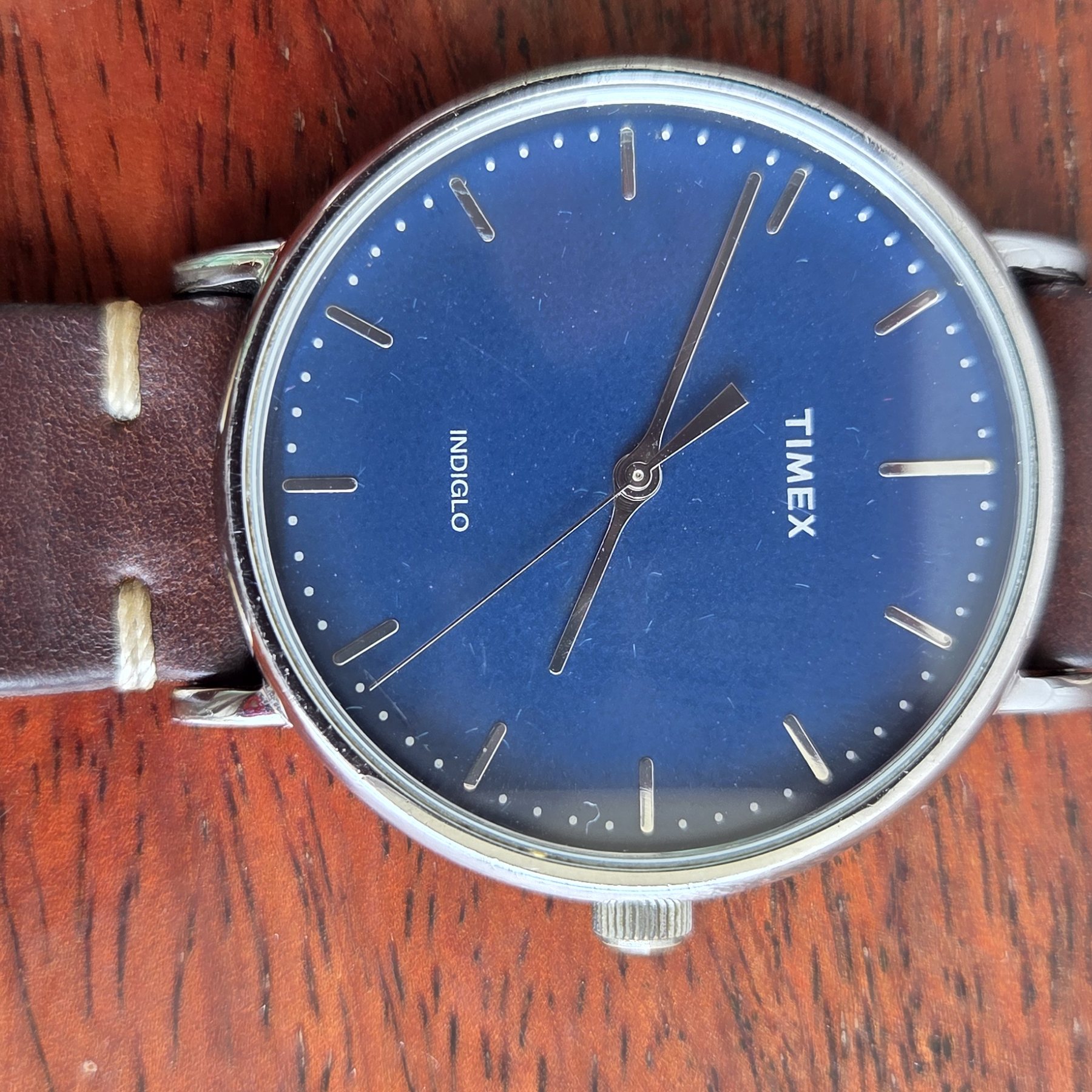 A Timex wristwatch with a deep blue dial and slim baton markers, on a brown leather strap.