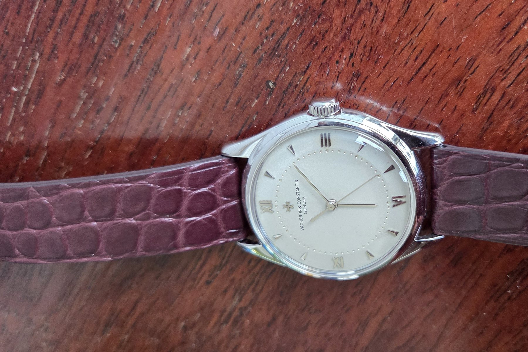 The whole watch laid out flat on a wooden table with its burgundy alligator strap extended.