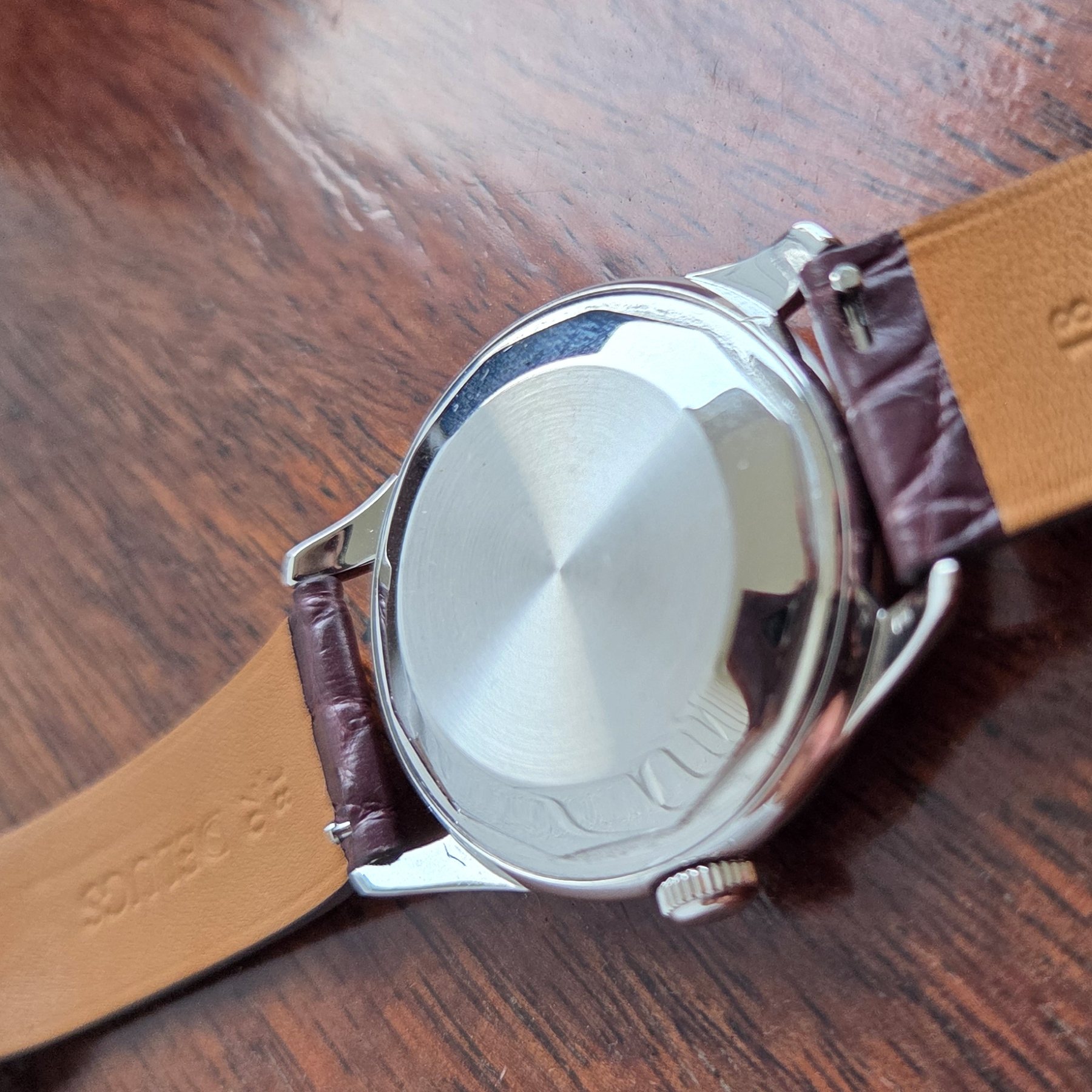 The case back at an angle, with the tan underside of the strap stamped 18mm Delugs.