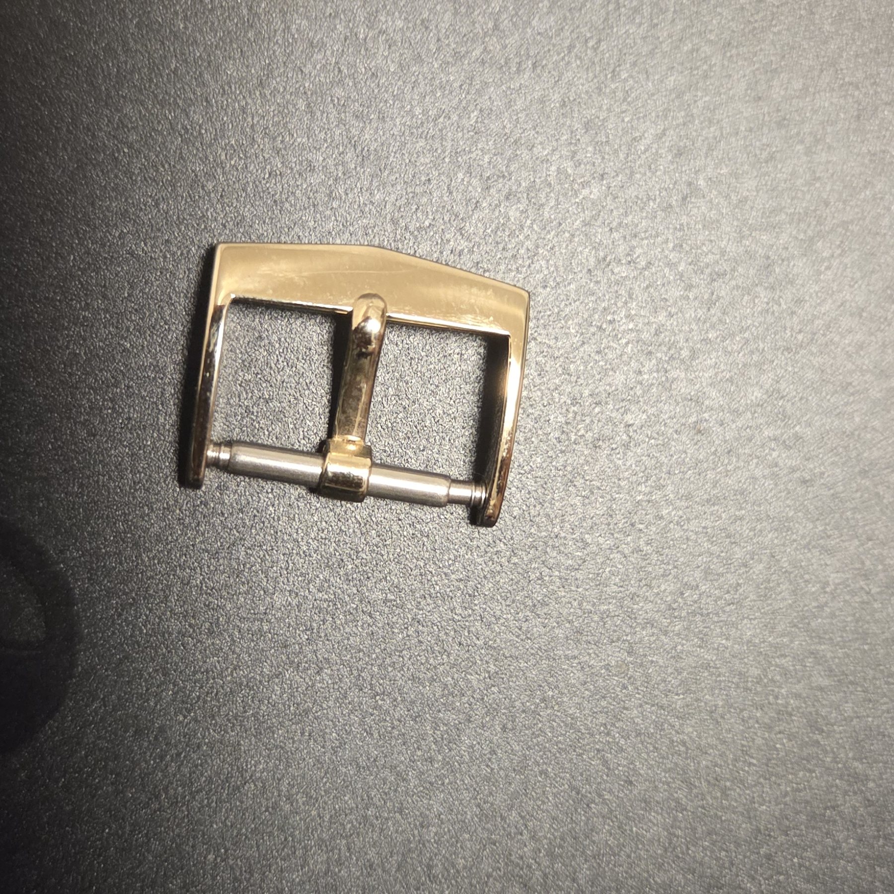 The signed gold buckle, photographed alone against a dark background.