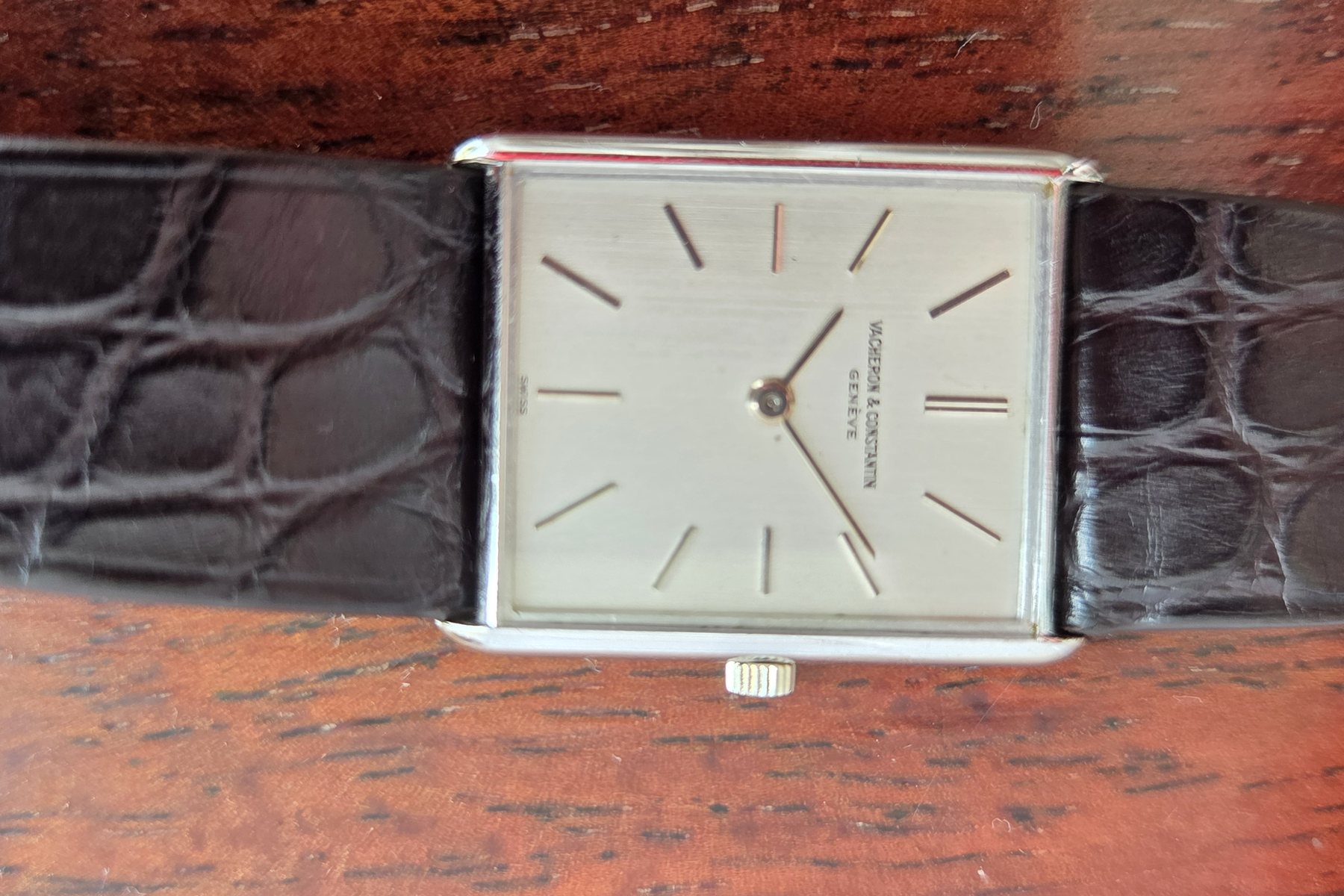 The watch on its black alligator strap, laid on a wooden table.