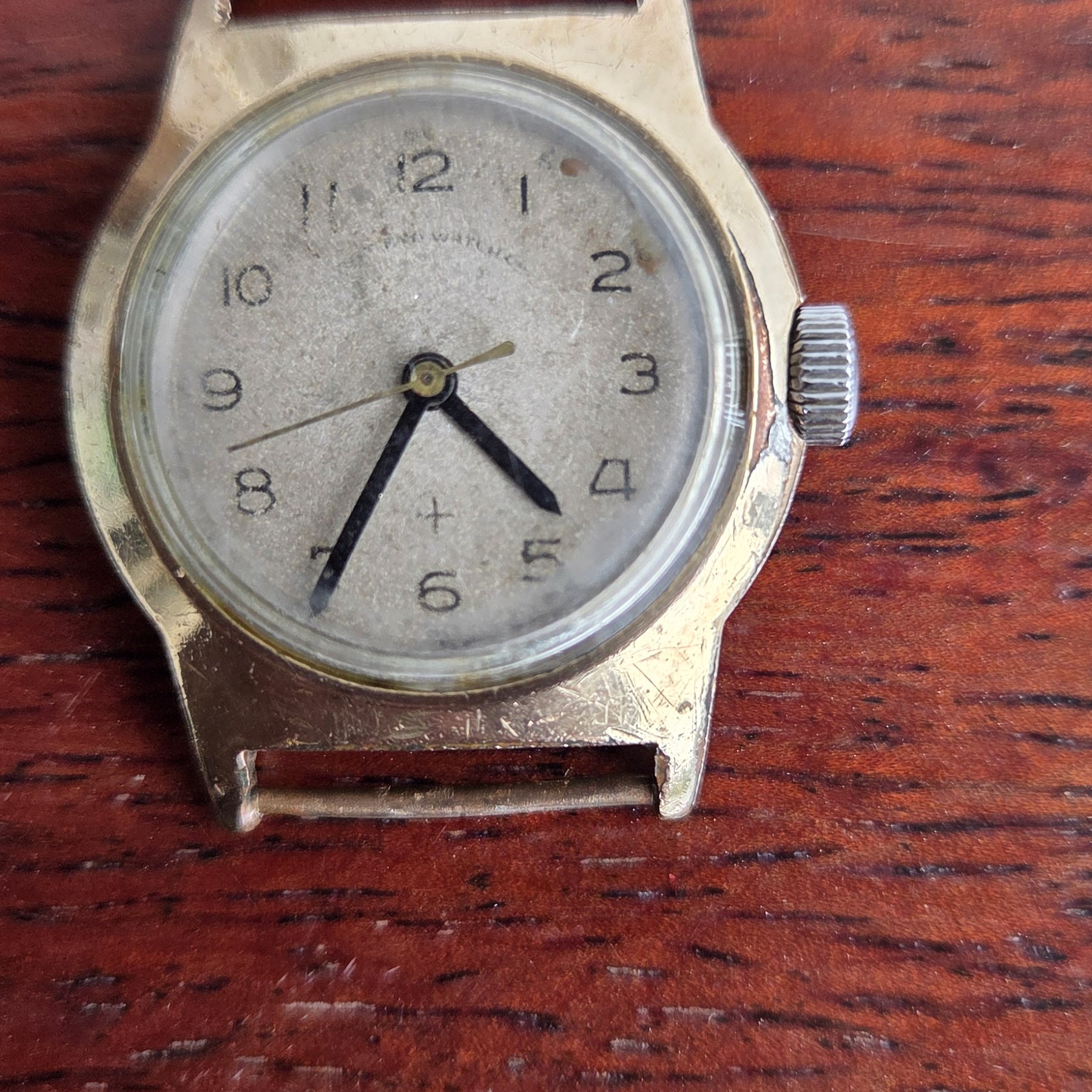 The watch with no strap fitted, laid face-up on a wooden table.
